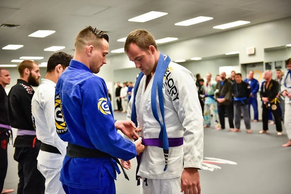 Coach tying a new belt on a student during a Glory belt promotion