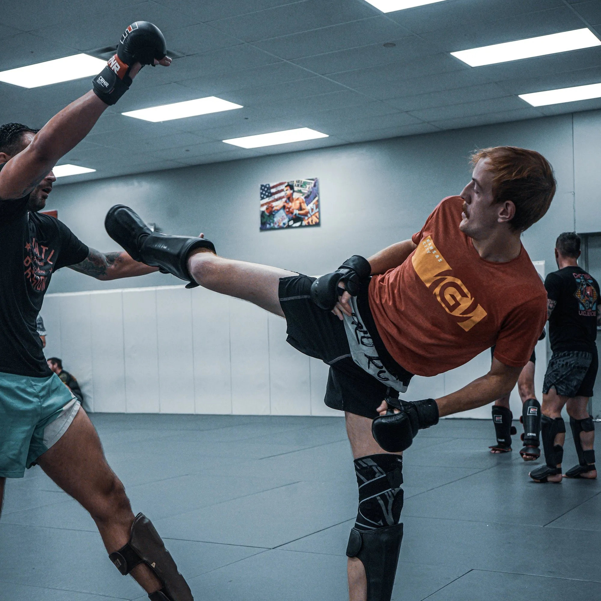 Student in a Glory shirt throwing a high kick into a coach's shield