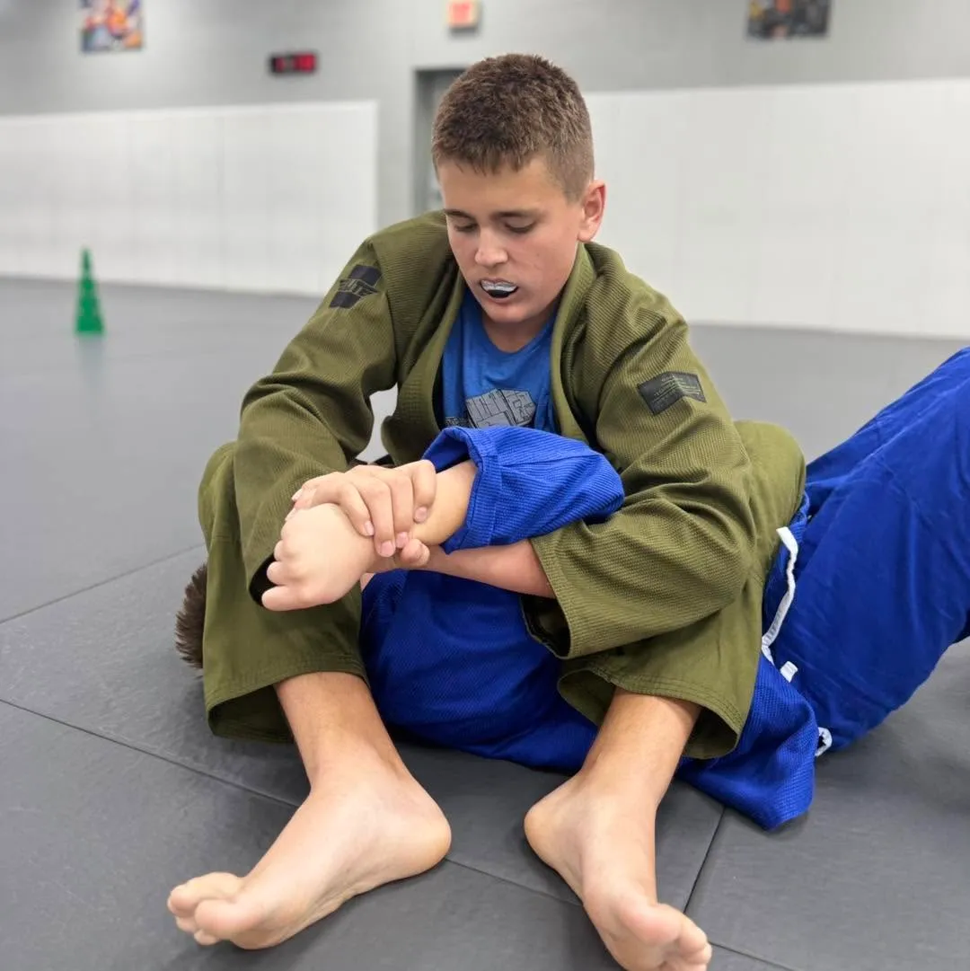 Young grappler in an olive gi controlling his partner's arm